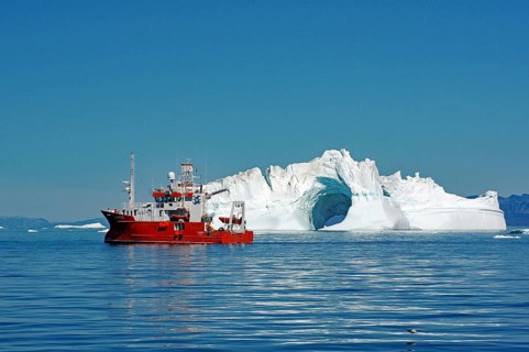 Red research vessel in front of iceberg with LOch