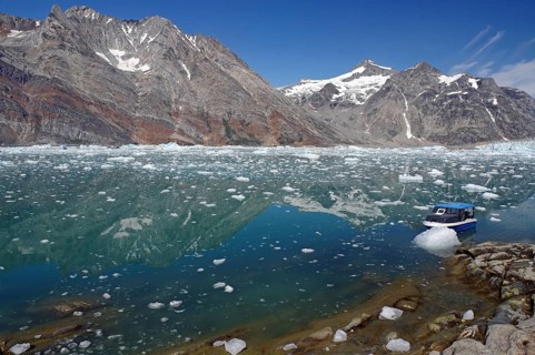 Blue boat in a calm fjord covered with pieces of ice