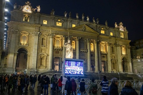 Faithful Christians outside St. Peter's Basilica watch Pope's Mass on large monitor at night