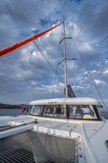 Recessed headsail and deck with net of a sailing catamaran in evening light