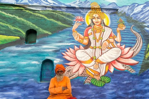 Sadhu in saffron robes in front of an image of a deity