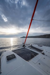 Recessed headsail and deck with net of a sailing catamaran in evening light