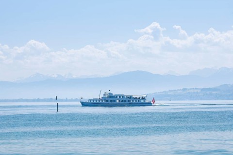 View from Arbon over the shimmering blue Lake Constance with a scheduled boat in sunny weather and blue sky in summer