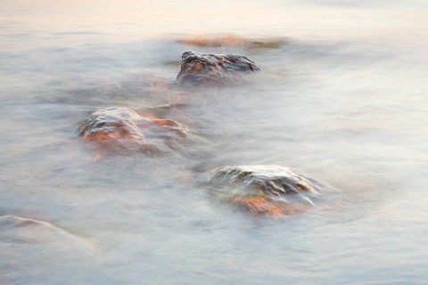 Light play and stones in the water at sunrise photographed with slow shutter speed