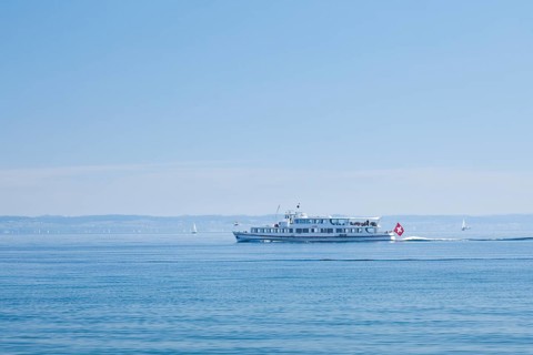 View from Arbon over the shimmering blue Lake Constance with a scheduled boat in sunny weather and blue sky in summer