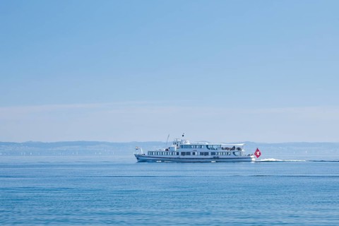 View from Arbon over the shimmering blue Lake Constance with a scheduled boat in sunny weather and blue sky in summer