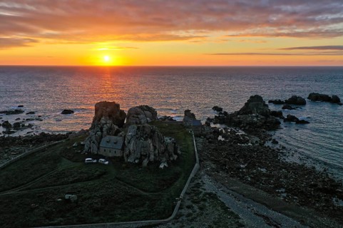 Drone shot from the mainland of the house between the rocks (Le gouffre de Plougrescant) and the Atlantic Ocean at sunset