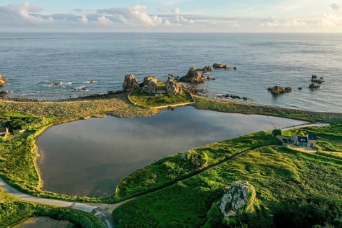 Drone shot from the mainland of the granite coast and the house between the rocks (Le gouffre de Plougrescant) in the morning and the Atlantic Ocean