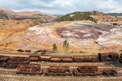 Disused wagons at the dramatically scarred landscape of mineral-rich ground and rock at the Rio Tinto mines