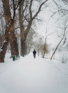 Solitary man silhouette wandering a snowy walkway in the winter park. Calm and moody scene