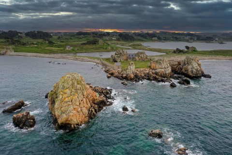Drone shot from the Atlantic Ocean onto the granite coast of Plougrescant with a view of the house between the rocks (Le gouffre de Plougrescant) at sunset