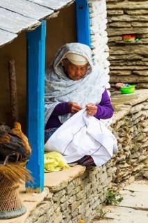 Elderly Nepalese woman sitting in the doorway sewing