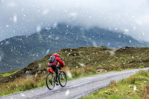 Lone cyclist on heavily laden touring bike on single track road through the Scottish Highlands in spring sleet