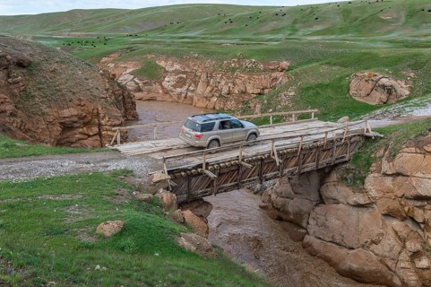Off-road vehicle crossing a wooden bridge over a wild gorge