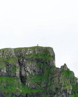 A person stands on a cliff in the distance