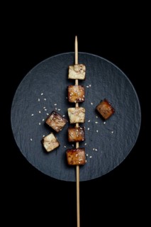 Fried tofu cubes with wooden skewer on plate