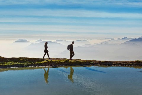Hikers on a small lake with the peaks of the Lake Garda mountains and Bergamo Alps