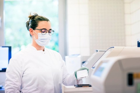 Young lab technician with mouth guard and sample multilayer shell working in a lab with lab equipment