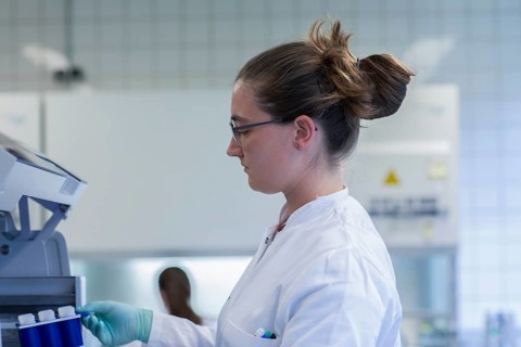Young lab technician wearing a face mask and pipetting a sample in a laboratory with laboratory equipment at a workflow