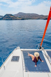 Young woman with hat sitting in the net of a sailing catamaran