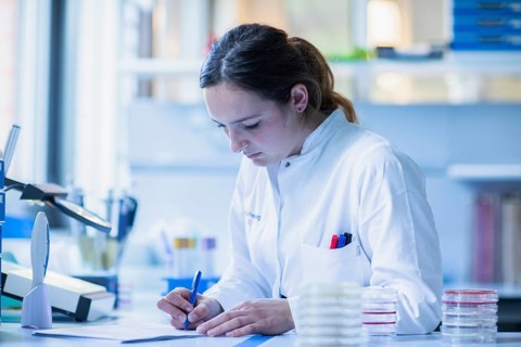 Lab technician with sample in petri dish works in a lab with lab equipment and writes protocol