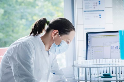 Young chemist with sample and laboratory glasses working in a laboratory with laboratory equipment and monitor