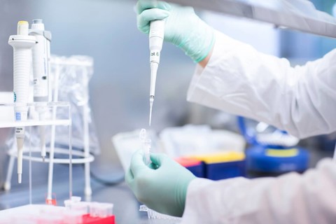 Young lab technician wearing a face mask and pipetting a sample in a laboratory with laboratory equipment at a workflow