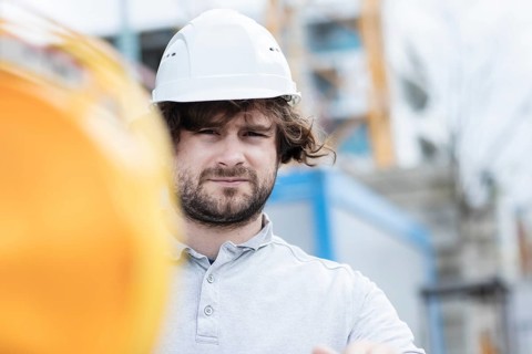 Technician with beard middle aged and wearing polo shirt and helmet outside at work