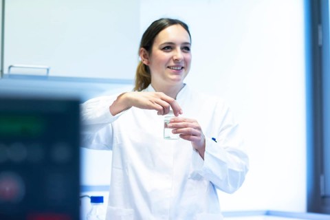 Young laboratory assistant with sample and laboratory glasses working in a laboratory with laboratory equipment