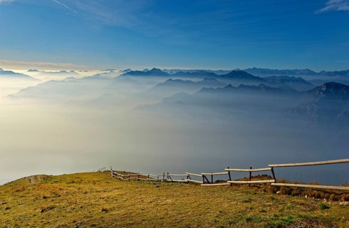 Meadow with fence and Lake Garda in the morning mist with Lake Garda mountains and Bergamo Alps