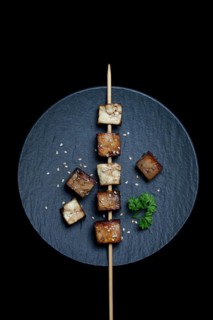 Fried tofu cubes with wooden skewer on plate