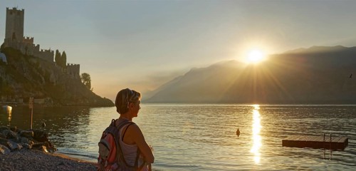 Hiker on the shore in front of Castello Scaligero at sunset