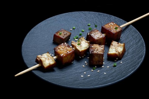 Fried tofu cubes with wooden skewer on plate