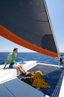 Young man sitting in the net of a sailing catamaran