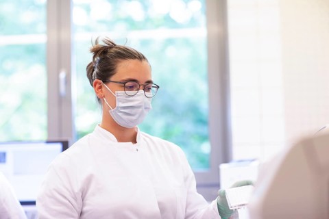 Young lab technician with mouth guard and sample in tubes working in a lab with lab equipment