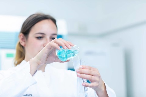 Young laboratory assistant with sample and laboratory glasses working in a laboratory with laboratory equipment