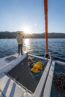 Young man standing on a catamaran looking into the sunset