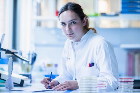 Lab technician with sample in petri dish works in a lab with lab equipment and writes protocol