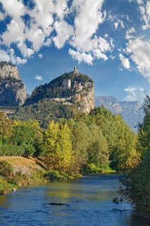 Small idyllic river Sarca with the medieval castle ruin Castello di Arco towering on a castle rock