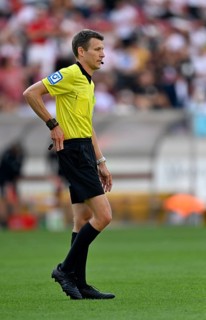 Referee Benjamin Cortus reaches into right hip pocket and pulls out red card