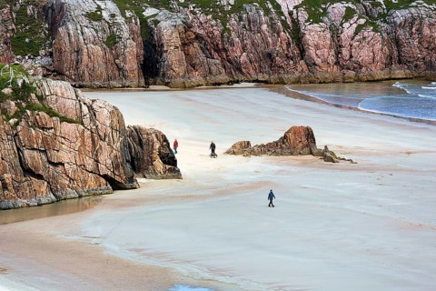 Walkers in bay with rocks and sandy beach