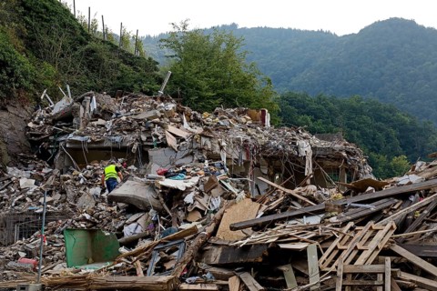 A man in mountains of rubble and rubbish in front of the Ahr mountains