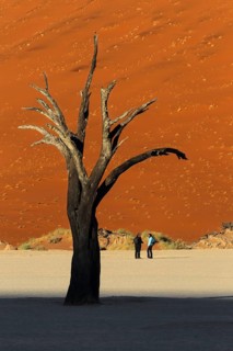 A group of 3 tourists stand on the Deadvlei clay pan together. Deadvlei
