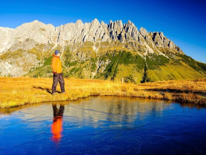 Mountaineer in front of mountain scenery reflected in a frozen mountain lake
