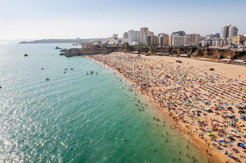 Aerial view of touristic Portimao with wide sandy beach Rocha full of people