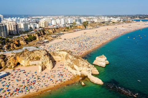 Aerial view of touristic Portimao with wide sandy beach Rocha full of people