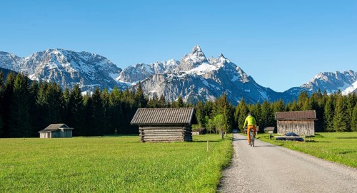 Mountain biker on road through meadow with hay barns