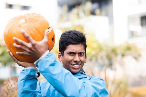 Young man with blue jacket and big pumpkin outside