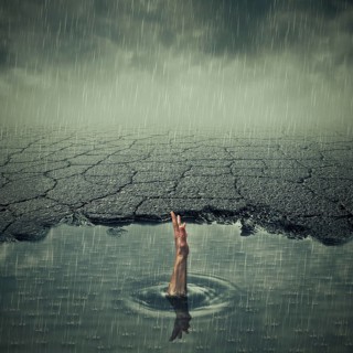 Surrealistic image with a single hand of drowning man asking for help in a pothole of cracked asphalt