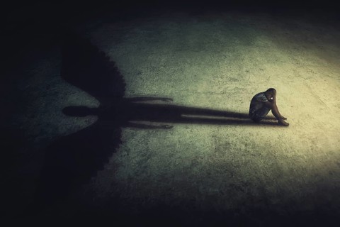 Depressed young man sitting alone isolated in a dark room